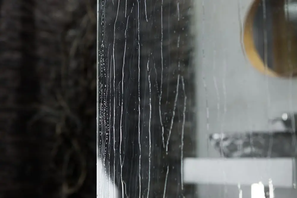 Rayas de minerales secos que quedan en el vidrio de la regadera después de limpiar — los depósitos que los productos caseros no pueden quitar